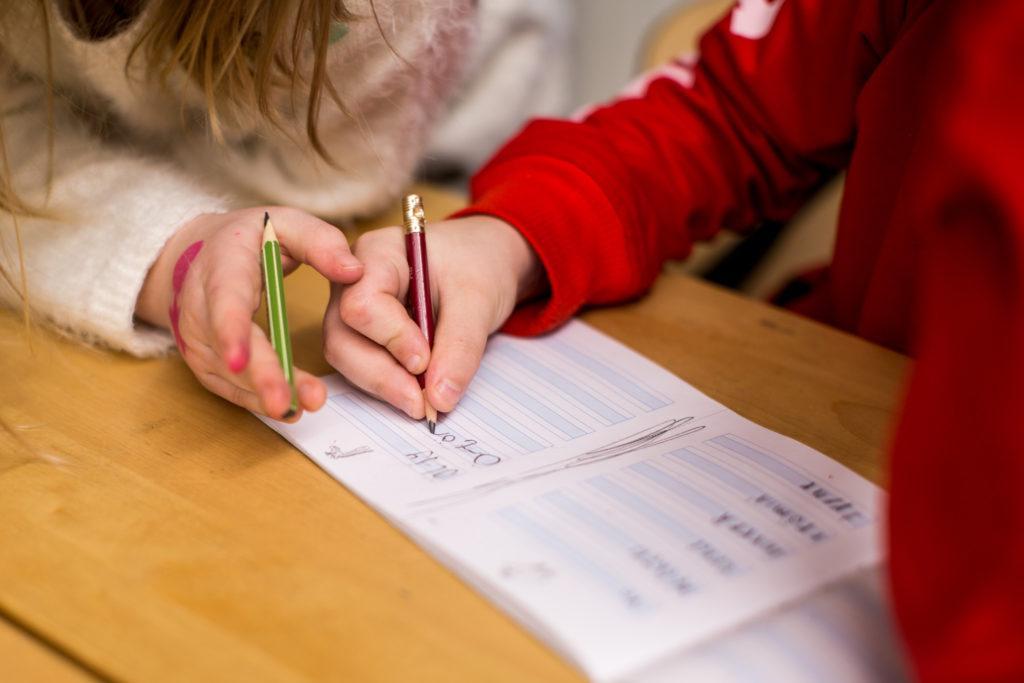Koululaiset tekevät vihkoon käsialaharjoituksia.