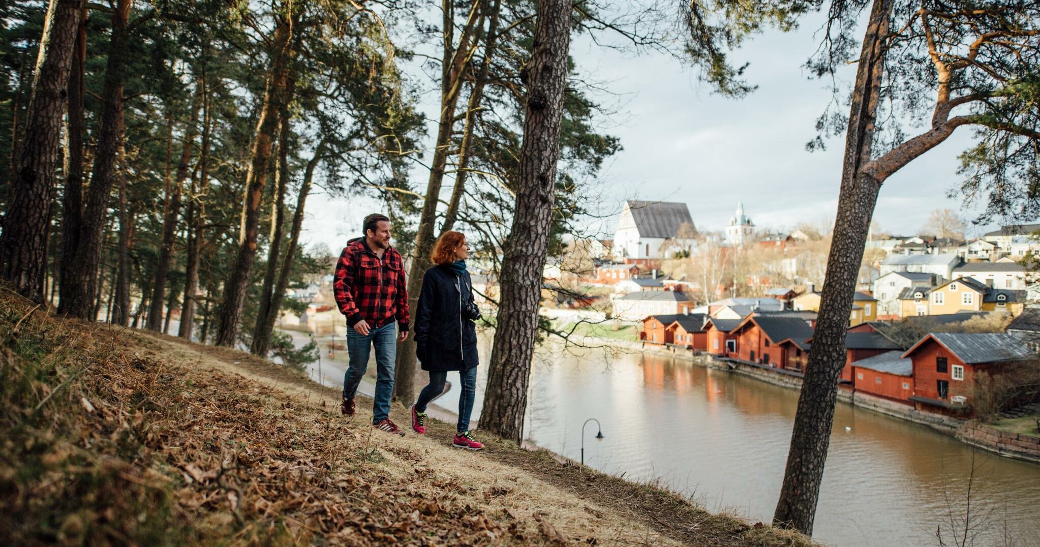 En man och en kvinna promenerar längs åstranden med strandbodarna på bakgrund.