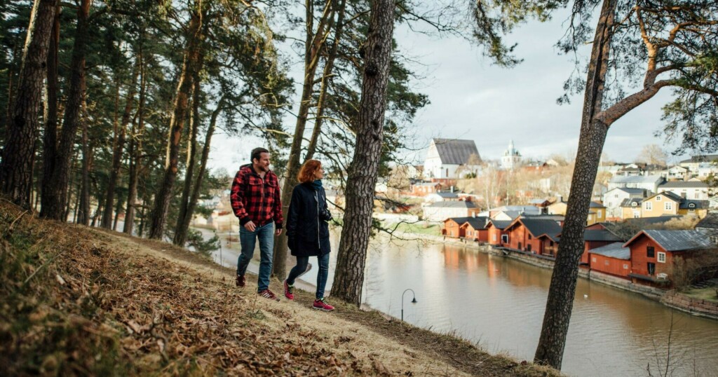 Mies ja nainen kävelevät syksyisessä metsässä, Porvoon ranta-aitat taustalla.