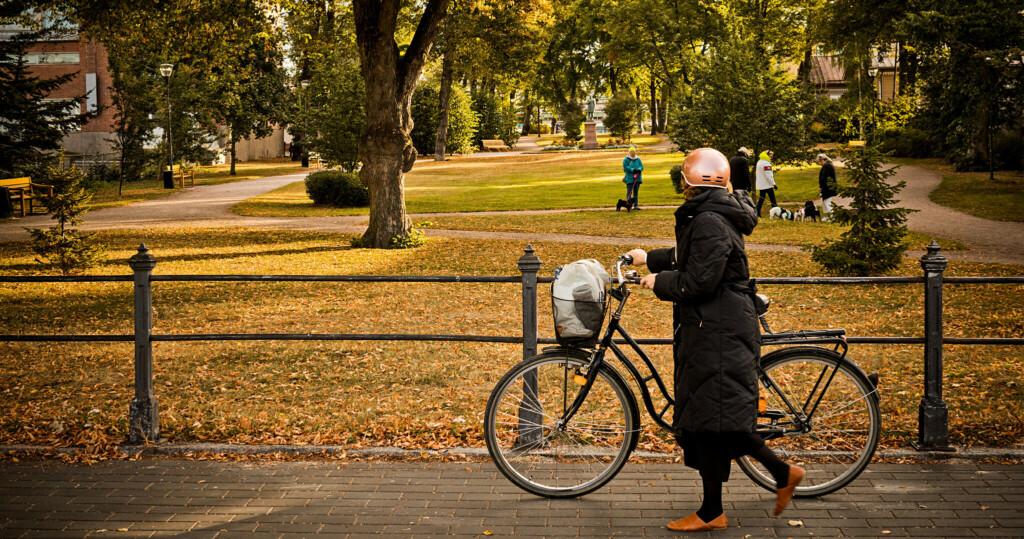 Nainen taluttaa pyörää Runebergin puistossa.