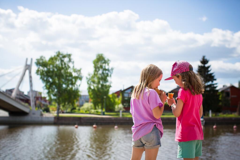 Lapset syövät jäätelöä Porvoon joen rannalla.