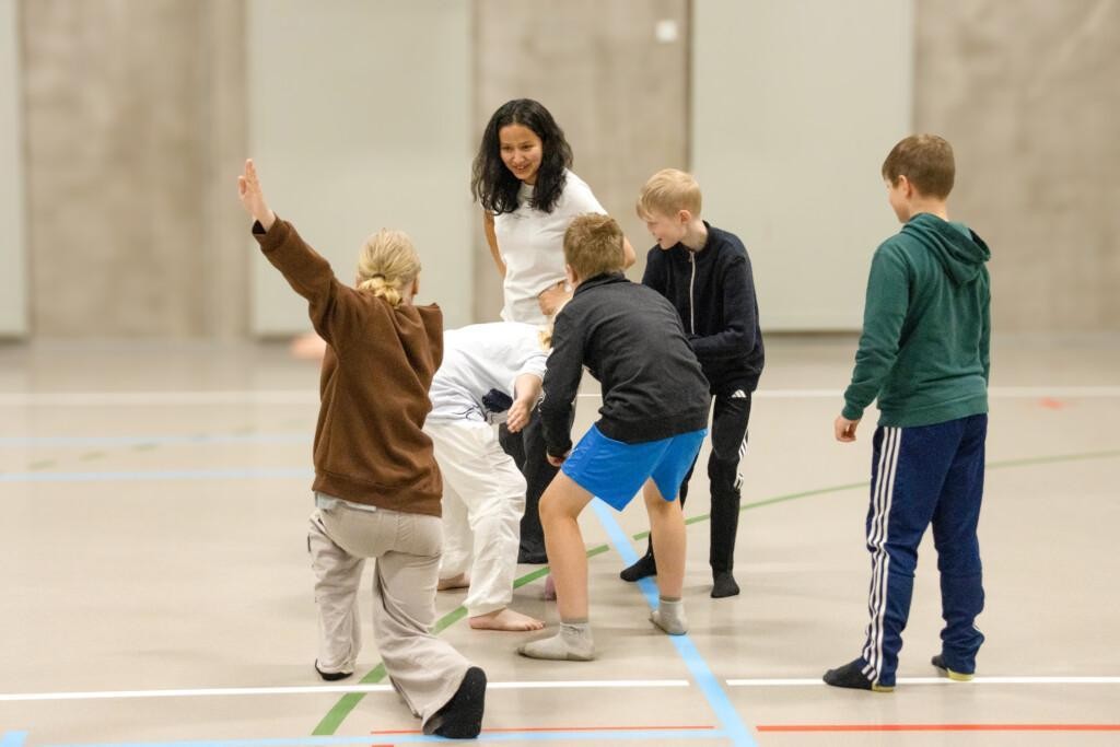 Barn leker i gymnastiksalen med en lärare.