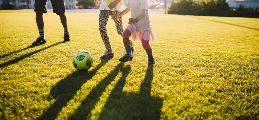 En familj spelar fotboll på gräsplan.