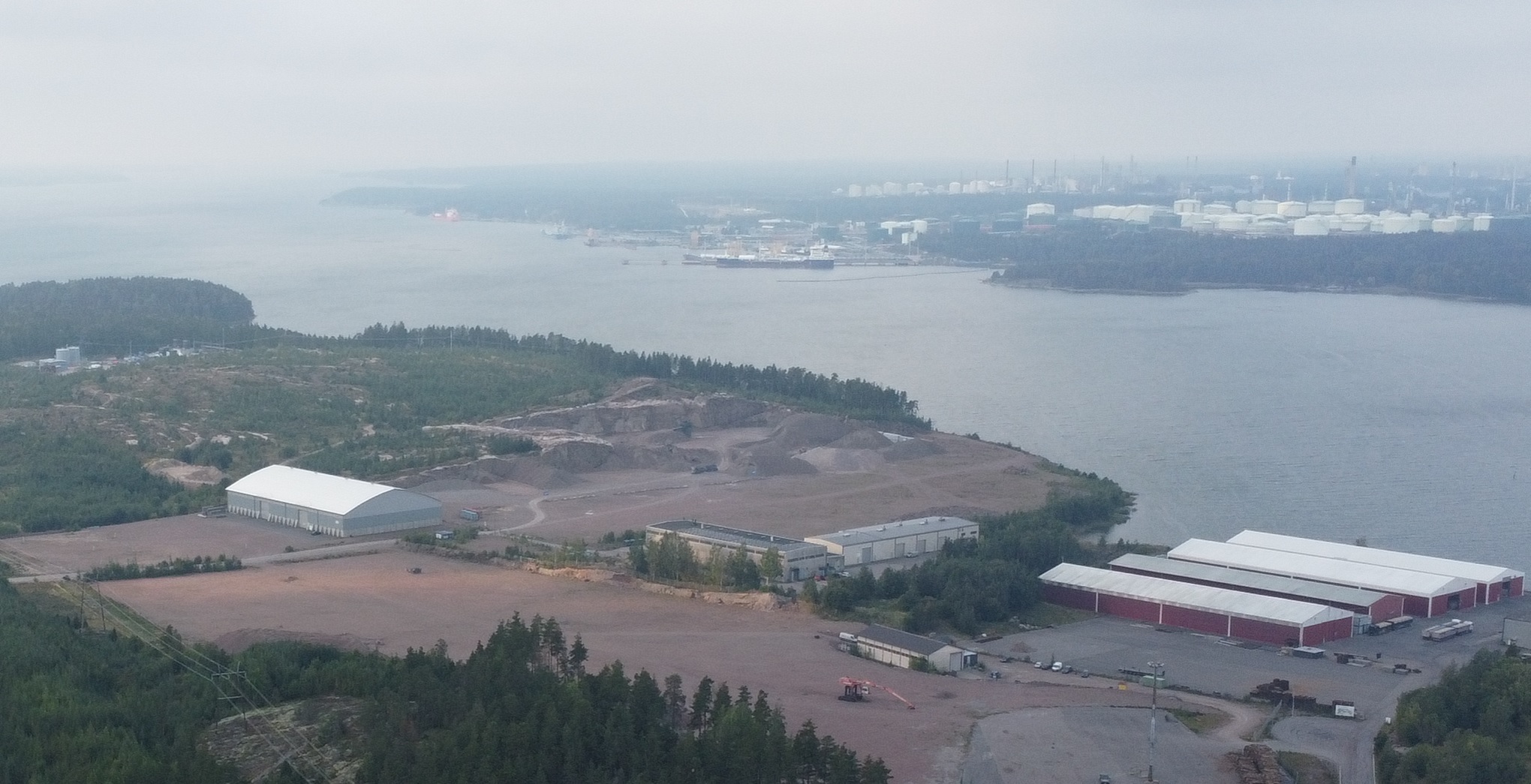 Ilmakuvassa Tolkkisen vetylaitoksen asemakaava-aluetta sekä viereisen tontin varastorakennuksia. Taustalla näkyy merenlahden takana Kilpilahden teollisuusalue. Kuva otettu elokuussa 2024.